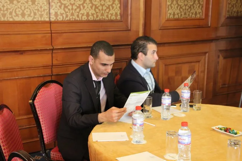 Walid reading a Tritux leaflet at a round table, with Fourat Zouari seated beside him