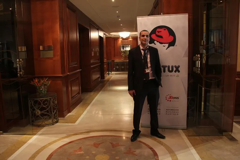 Walid standing in the hotel lobby in front of a Red Hat and Tritux roll-up banner