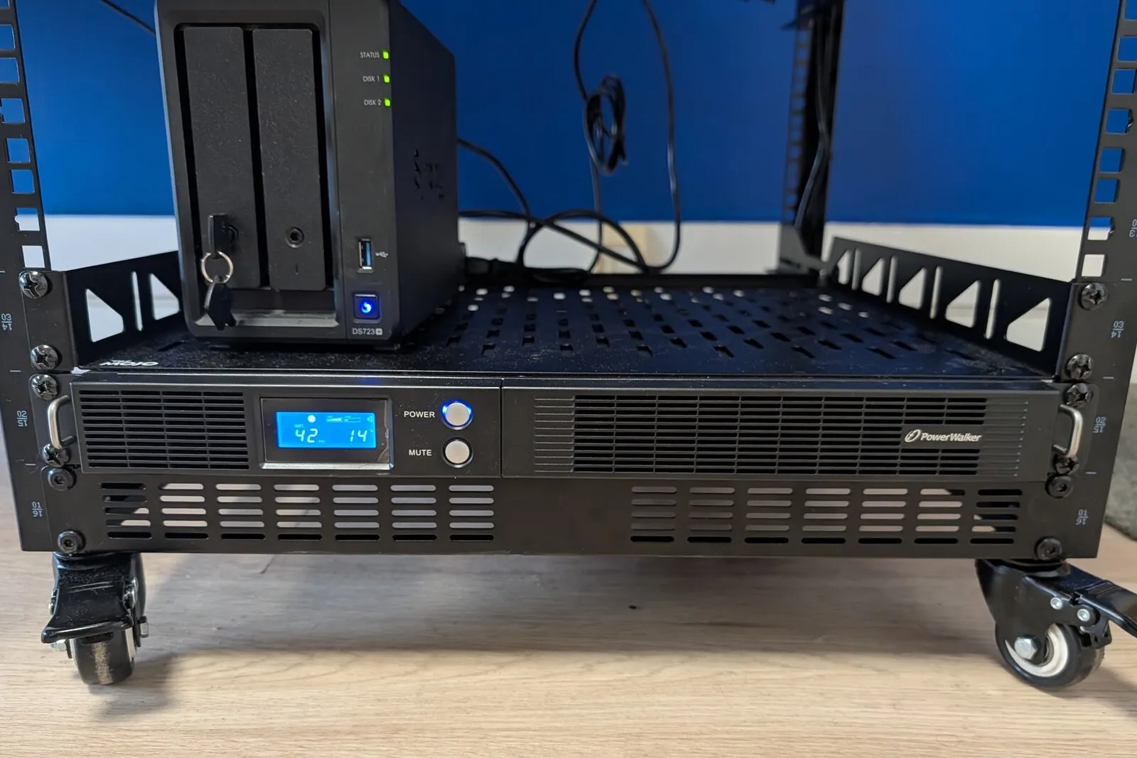 The PowerWalker VI 750 R1U UPS in the bottom 1U slot of the rack, its front display lit, with the Synology DS723+ NAS on the shelf above it